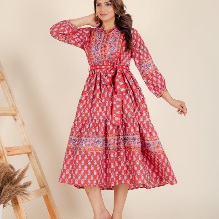 A woman in a red floral maxi dress and with long sleeve stand in front of a light color wall