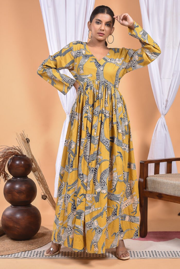 A woman in a, zebra-themed sexy yellow maxi dress with a gathered waist and halter neckline stands in front of a light orange wall with a white drape and a table with a brass vase and flowers.