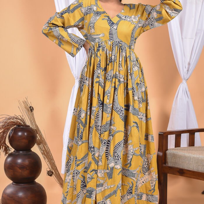 A woman in a, zebra-themed sexy yellow maxi dress with a gathered waist and halter neckline stands in front of a light orange wall with a white drape and a table with a brass vase and flowers.