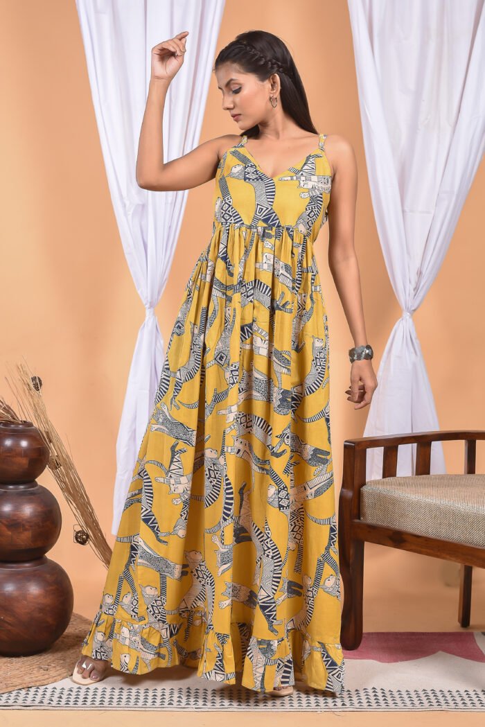 A woman in a, zebra-themed sexy yellow maxi dress with a gathered waist and halter neckline stands in front of a light orange wall with a white drape and a table with a brass vase and flowers.