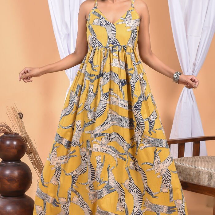 A woman in a, zebra-themed sexy yellow maxi dress with a gathered waist and halter neckline stands in front of a light orange wall with a white drape and a table with a brass vase and flowers.