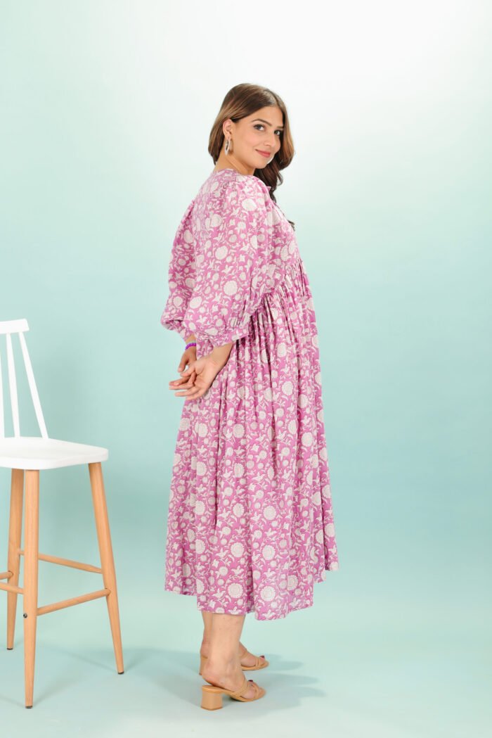 A woman in a pink floral maxi dress and with long sleeve stand in front of a light color wall