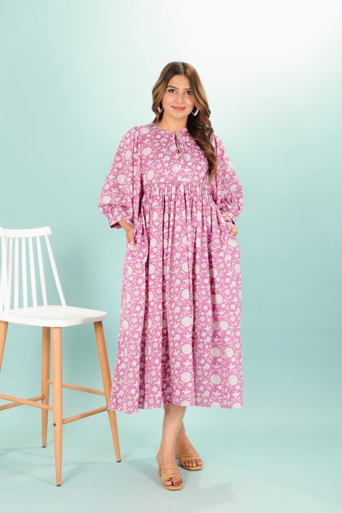 A woman in a pink floral maxi dress and with long sleeve stand in front of a light color wall