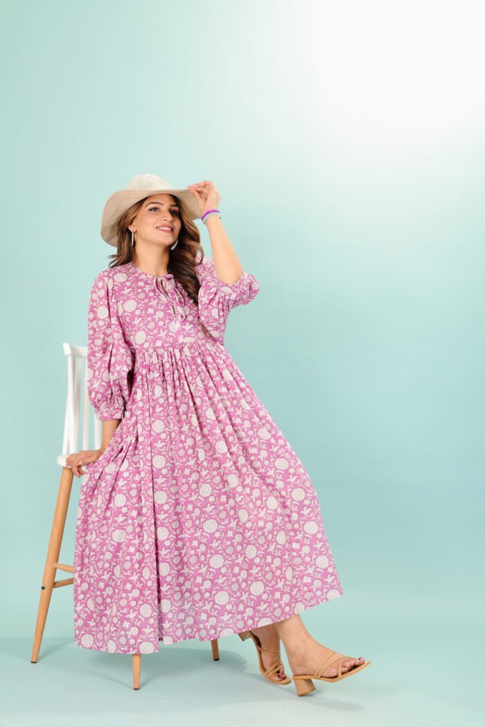 A woman in a pink floral maxi dress and with long sleeve stand in front of a light color wall