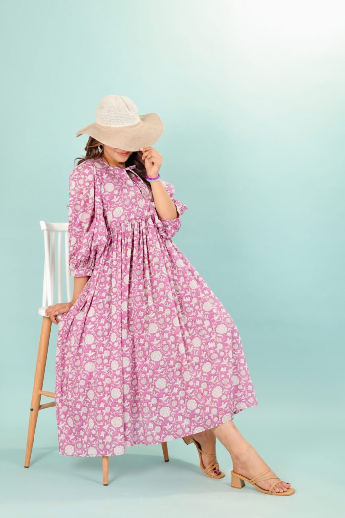 A woman in a pink floral maxi dress and with long sleeve stand in front of a light color wall