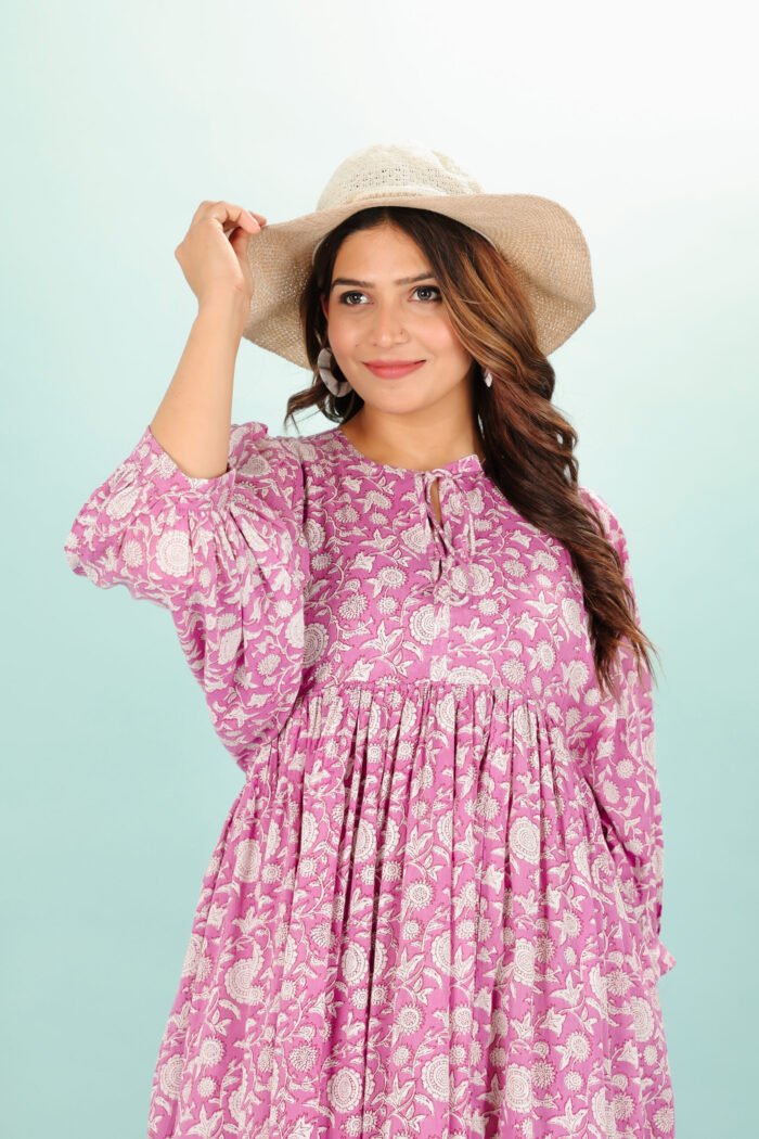 A woman in a pink floral maxi dress and with long sleeve stand in front of a light color wall