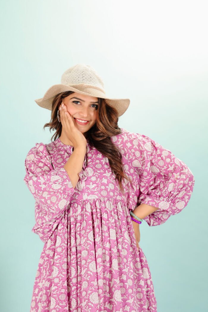 A woman in a pink floral maxi dress and with long sleeve stand in front of a light color wall