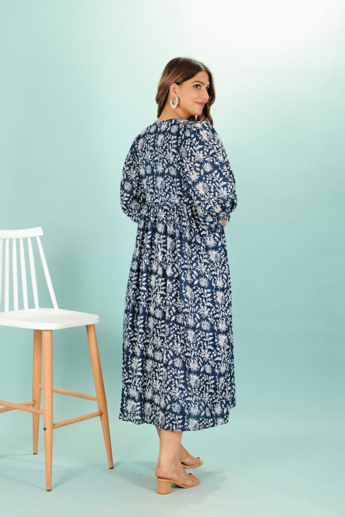 A woman in a black floral maxi dress and with long sleeve stand in front of a light color wall