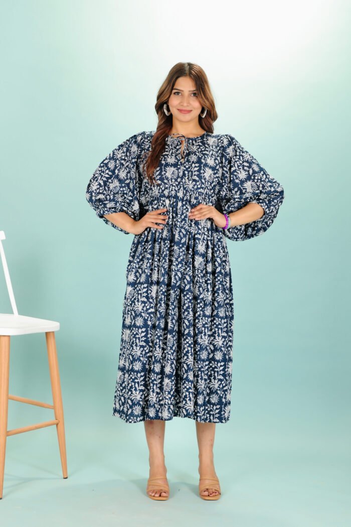 A woman in a black floral maxi dress and with long sleeve stand in front of a light color wall