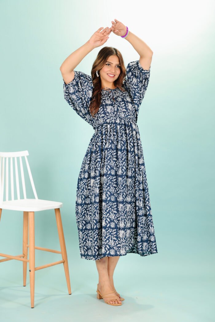 A woman in a black floral maxi dress and with long sleeve stand in front of a light color wall