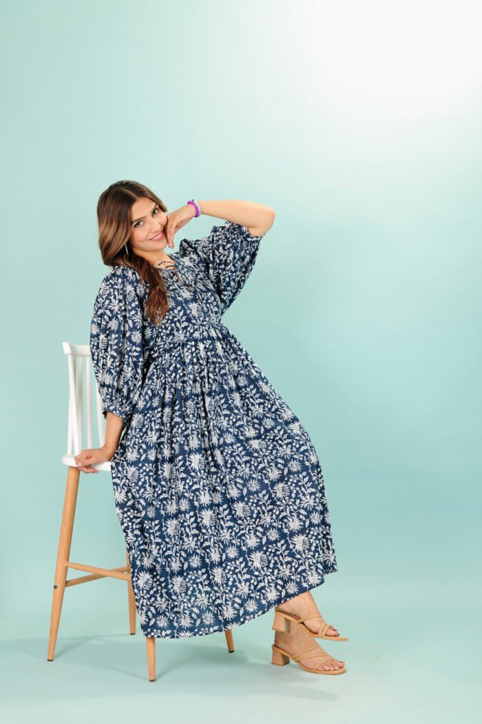 A woman in a black floral maxi dress and with long sleeve stand in front of a light color wall